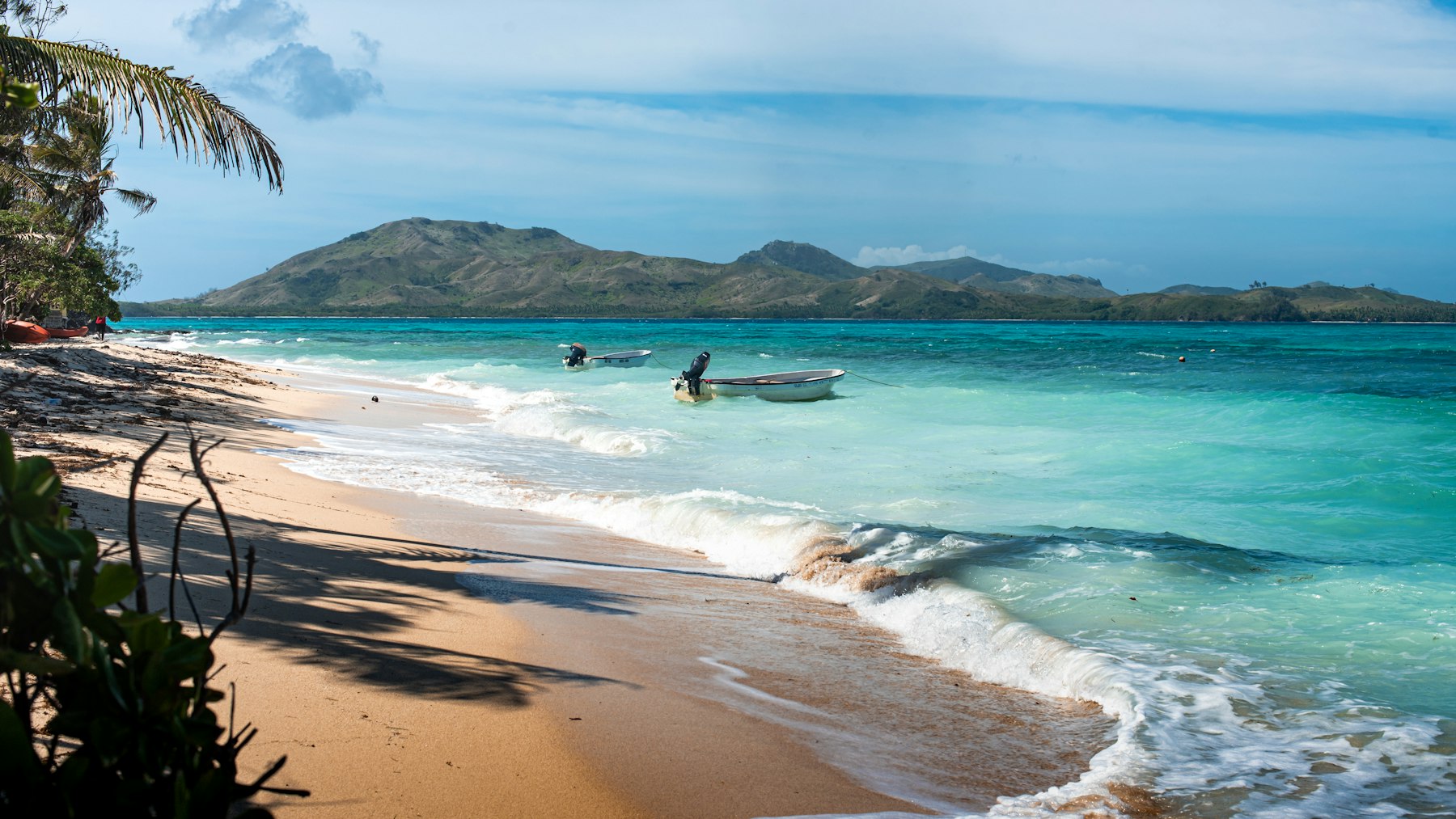 A quiet beach with a small boat in the water and a green headland behind.